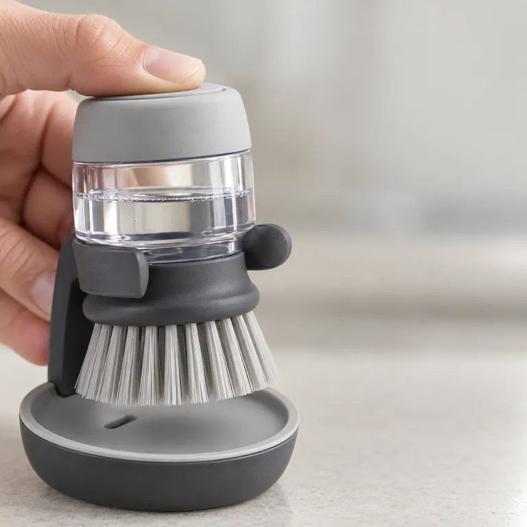 Close-up of a thumb pressing the grey top button of the brush above its clear soap reservoir.