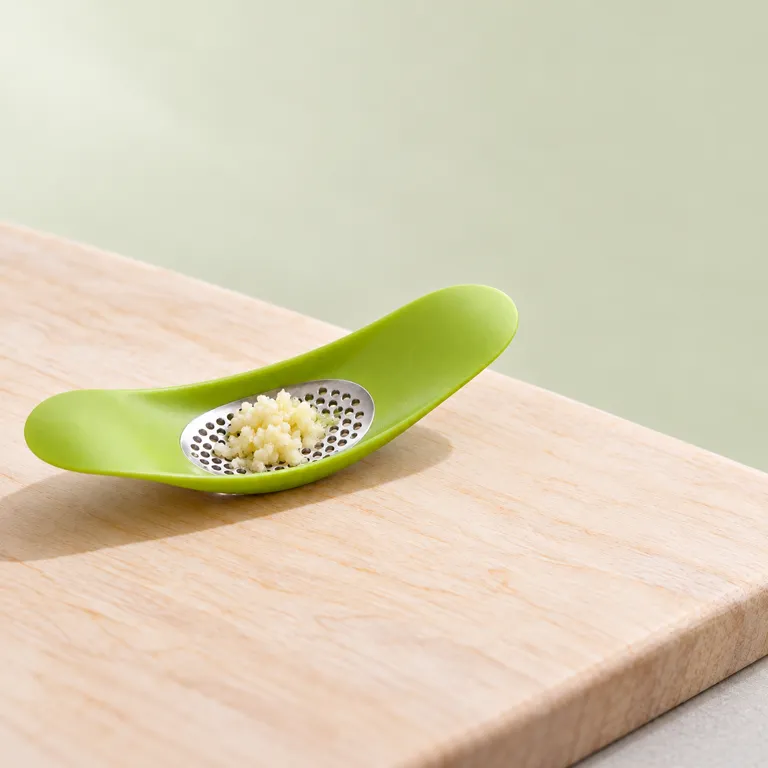 Macro view of crushed garlic gathered on the perforated plate in the green crusher's bowl-shaped top.