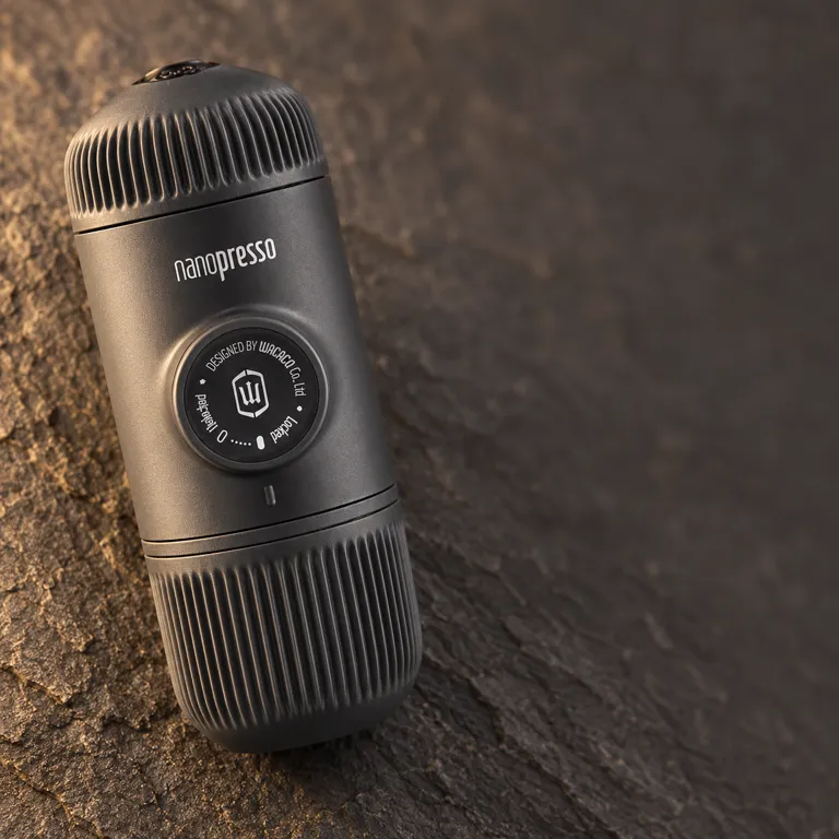 The charcoal espresso maker angled on dark stone, showing its round pumping knob with printed markings and its ribbed ends.